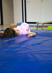 Pretty, light-eyed girl lying on mats in her school gymnasium.