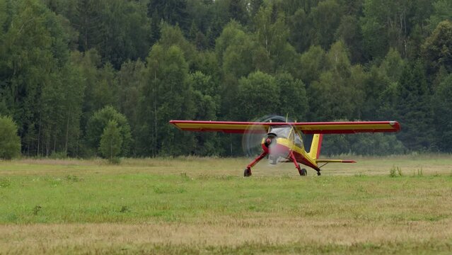 small bright yellow-red civilian small aircraft accelerates across field and is ready to take off. propeller plane on runway with trees in background is about to fly.