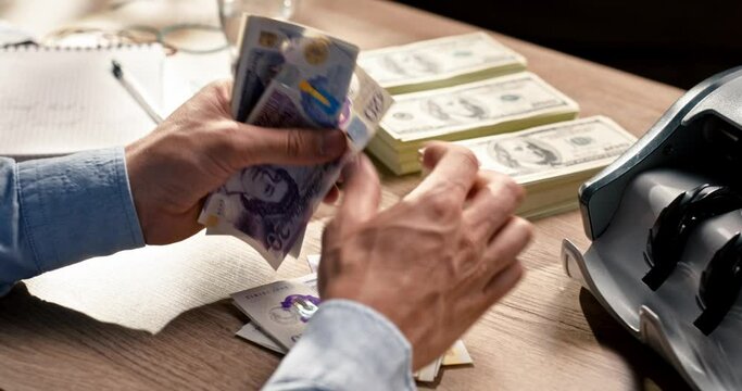 Man counting pouns bills sitting at desk indoors. Bankir calculating UK currency at work at table. Financial operations , loan credit. Male hands count cash money. Rich. Business concept