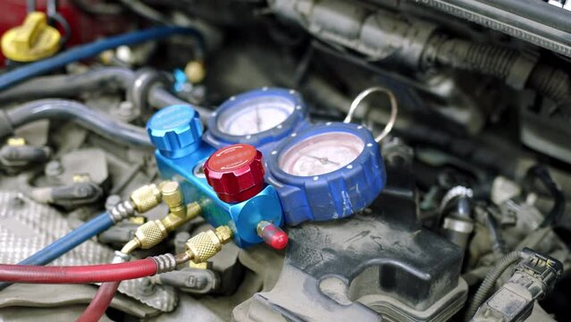 Under hood of open car lies system of manometers for refueling air conditioner. Blue pressure gauges with red and blue knobs in process of service maintenance of vehicle system.