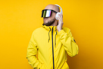 Young man in cyberpunk glasses in a yellow jacket with headphones on a yellow background