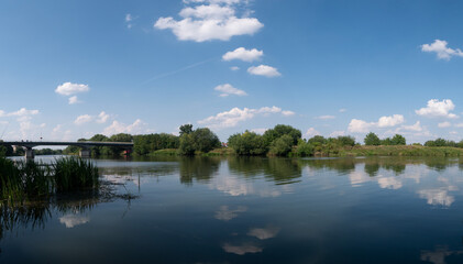 Fototapeta na wymiar Rzeka Odra, w tle most lekko pochmurna pogoda, błękit nieba zieleń przy brzegu, pora letnia, Odra w odcinku województwa Opolskiego