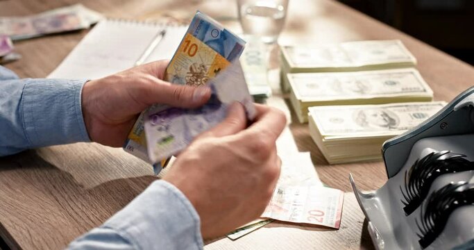 Close up of male accountant counting many banknotes while sitting at desk in cabinet. Male hands holding a lot of swiss krona cash at table. Business. Money concept. Bank and banking. Savings