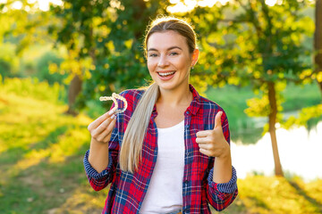 Attractive woman holding an invisible aligner braces on the street and shows a finger up. Dental...
