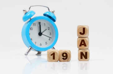 Wooden cube calendar for January 19, next to a blue alarm clock.