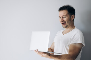 Guy programmer in a white t-shirt holds a laptop and smiles
