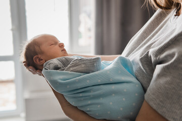 Portrait of newborn boy on mother's hand. Woman in front of the window looking at her newborn son. Baby boy sleeping in mother's arms. Selective focus. Film grain