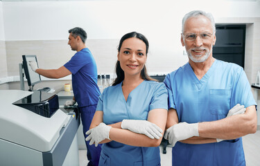 Portrait of laboratory workers with crossed arms standing in medical laboratory against background of modern laboratory research machines and equipment