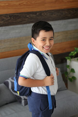 Hispanic male child ready for back to school with uniform and backpack takes his way to go to...