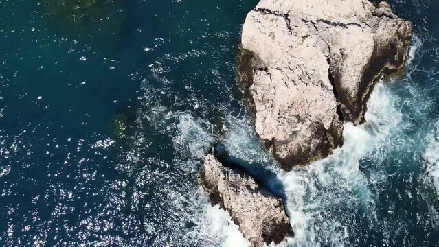 Waves makes white foam and crashing on rock seashore cliff at tropical island. Aerial Drone Shot of Sicily Italy. 4K Travel Footage Background. Small waves hitting the beach Sky aerial view over waves