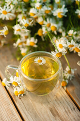 Cup of brewed chamomile tea on the background of a bouquet of daisies, close up.