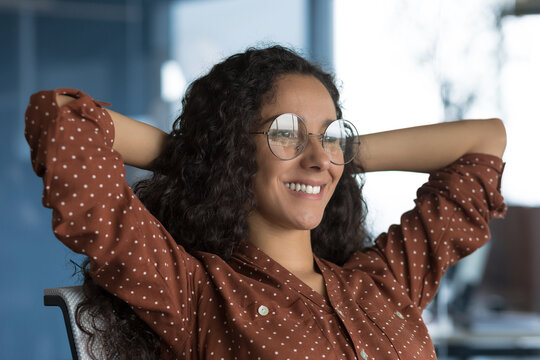 Young beautiful Arab business woman resting in the office smiling, female worker in glasses raised her hands on the title, resting and happy with success, close-up photo
