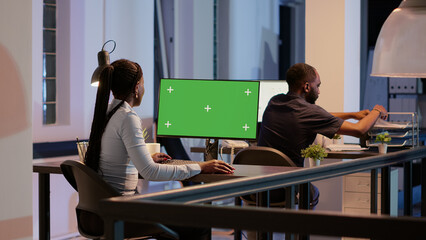 Business woman working with greenscreen on computer monitor, late at night. Analyzing isolated chroma key background with blank mockup template and copyspace display in modern office.