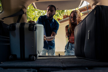 Man and woman loading baggage in vehicle trunk, leaving on summer holiday together. Couple...