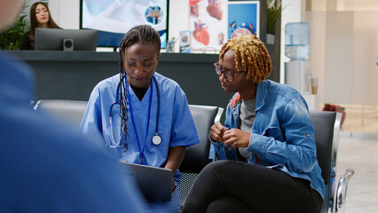 Obraz premium Female nurse and patient looking at laptop to find diagnosis, doing consultation in clinical reception lobby. Medical assistant explaining disease and treatment to woman in waiting room.