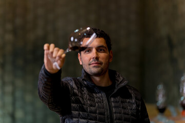 Man in the wine cellar with barrels in background drinking and tasting wine.