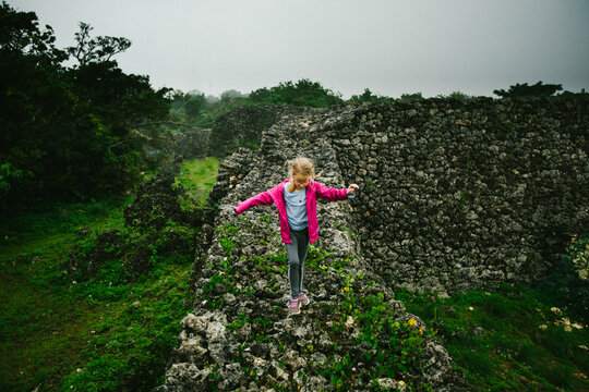 Girl child walks along castle ruin wall in tropical forest