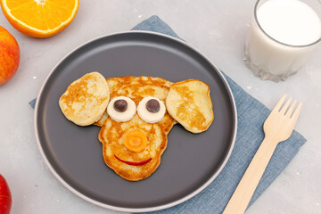 Funny monkey,dog face shape snack from pancake on plate. Cute kids childrens baby's sweet dessert, healthy breakfast,lunch, food art with milk,apples,orange on gray concrete background,top view