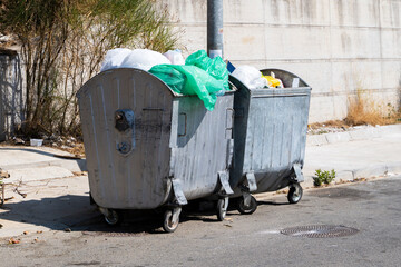 Metal dumpsters on the road in the city are full of all sorts of garbage. Human pollution....