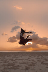 Silhouette of a happy woman jumping and having fun on the beach during sunset.  Freedom, vacation and leisure.