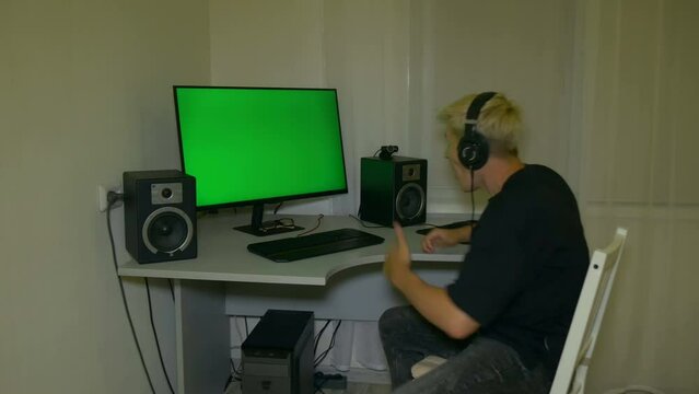 Guy is very happy with what is shown on the computer screen. Headphones on the head. Chromakey on computer screen. Video with a chroma key on the screen to insert any video or image.