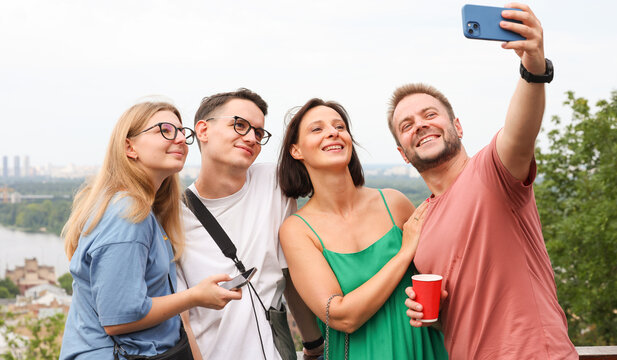 a company of friends uses a smartphone takes a selfie on the background of the city panorama.