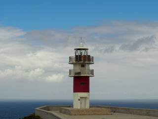 Fototapeta na wymiar A lighthouse in the cliff with the clouds and the ocean in the background.
