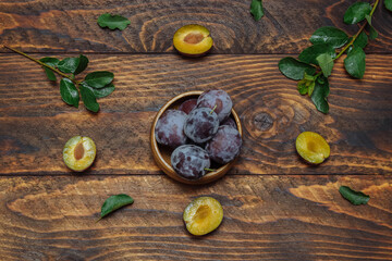 Ripe, juicy plums in bowl on brown wooden background with green leaves water drops, close-up, flatlay, rustic style, organic and veggie food concept, harvest season, ingredients for desserts, fructose