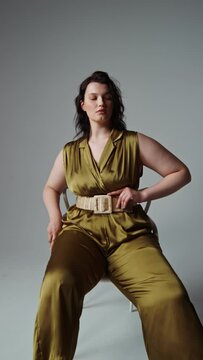 Plus size model posing sitting on a chair on a monochrome background in the studio, vertical video