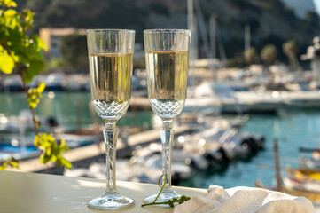 Pouring in two glasses of French champagne sparkling wine and view on colorful fisherman's boats in old harbour in Cassis, Provence, France