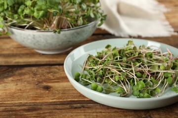 Plate with fresh radish microgreens on wooden table, space for text