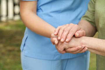 Elderly woman and female caregiver holding hands outdoors, closeup