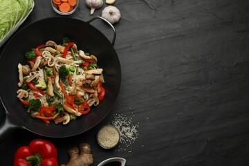 Stir fried noodles with mushrooms, chicken and vegetables in wok on black table, flat lay. Space...
