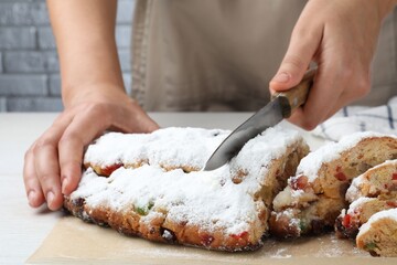 Woman cutting traditional Christmas Stollen with icing sugar at white wooden table, closeup