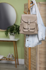 Fototapeta na wymiar Stylish beige backpack and jacket hanging on clothes rack indoors