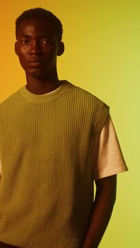 A man in a knitted vest looks seriously at the camera in the studio, vertical video