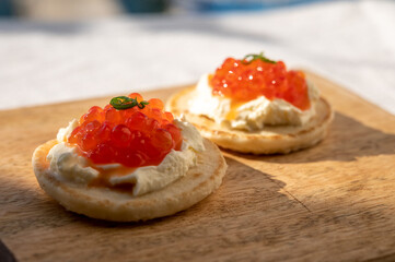 Two small starters blinis with sour cream and salted salmon red caviar served on mango tree wooden board