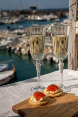 Pairing of blinis with sour cream and salted salmon red caviar and French champagne brut sparkling wine and served with view on colorful boats in harbor of Cassis, Provence, France