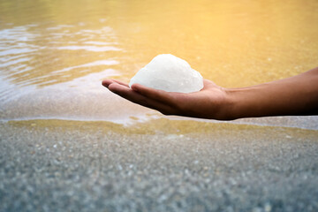 White alum bar holding in hand with cloudy water, concept for using alum to sway or swing the cloudy water to be clean and clear before using it in human daily life, soft and selective focus.