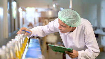Senior professional quality control officer inspecting the manufacturing line and computer system in the beverage bottling factory.