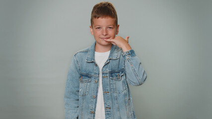 Call me, here is contact number. Toddler boy in jeans jacket looking at camera doing phone gesture...