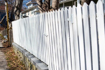 A stark white wooden picket fence enclosing a garden or yard with yellow leaves covering parts of...