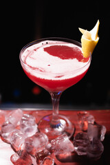 Red alcoholic cocktail on the bar, decorated with lemon and ice. The bartender prepares drinks for guests. Night life, club life. Great serving of cocktails. Amazing cocktails