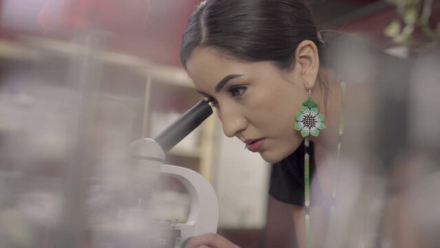 Close up of a Native American girl looking into the eyepiece of a microscope and then changing slides.
