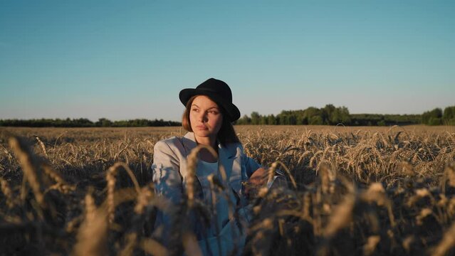 A cute girl is resting in a field at sunset. She winces a little from the sun as she turns her head