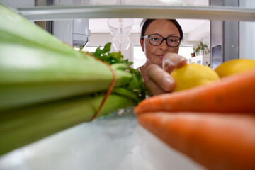 View from inside the fridge of middle aged woman taking out vegetables