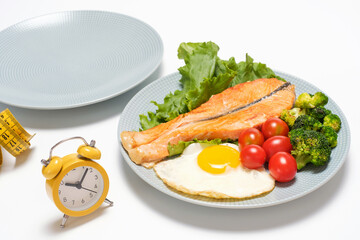 Two plates empty and with food and an alarm clock on white background, concept of intermittent fasting.