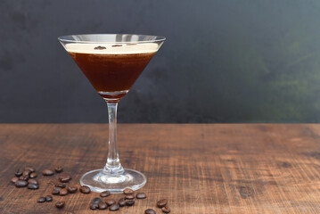 Glass of espresso martini with coffee beans on wooden table and black background