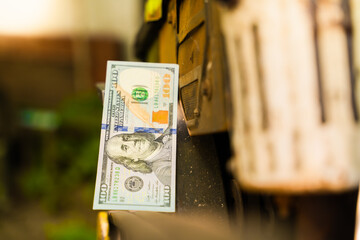 One hundred dollars lie on the belts of a tractor pulley close-up,blurred background. Money on...