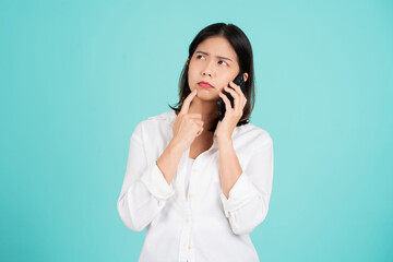 Portrait of young asian woman wearing white T-shirt on green background with dreamy look, thinking while holding smartphone. Tries to write up a message.